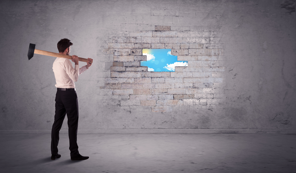 Business man hitting grungy brick wall with hammer